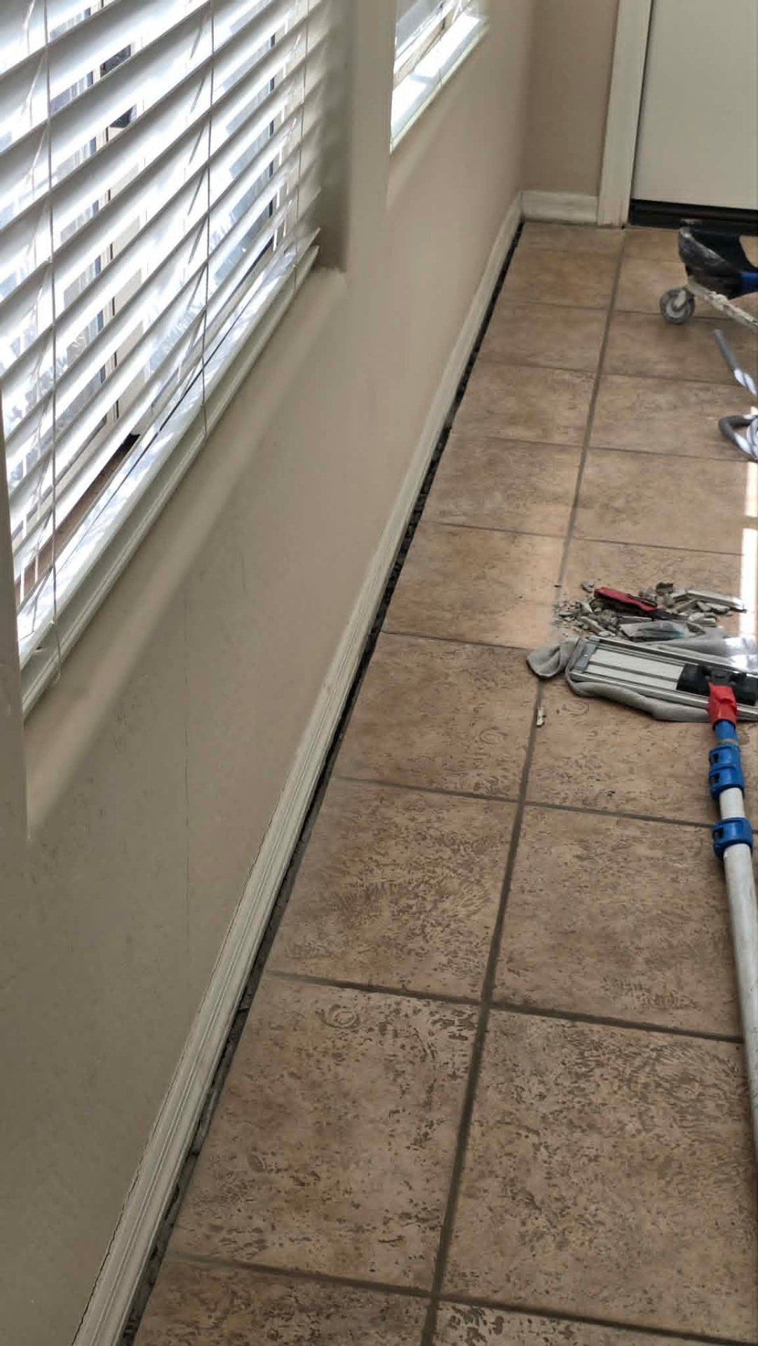 Tile repair in progress in Mesa AZ with baseboard shoe molding removed and the perimeter grout joint routed out along the wall to inspect the substrate before regrouting