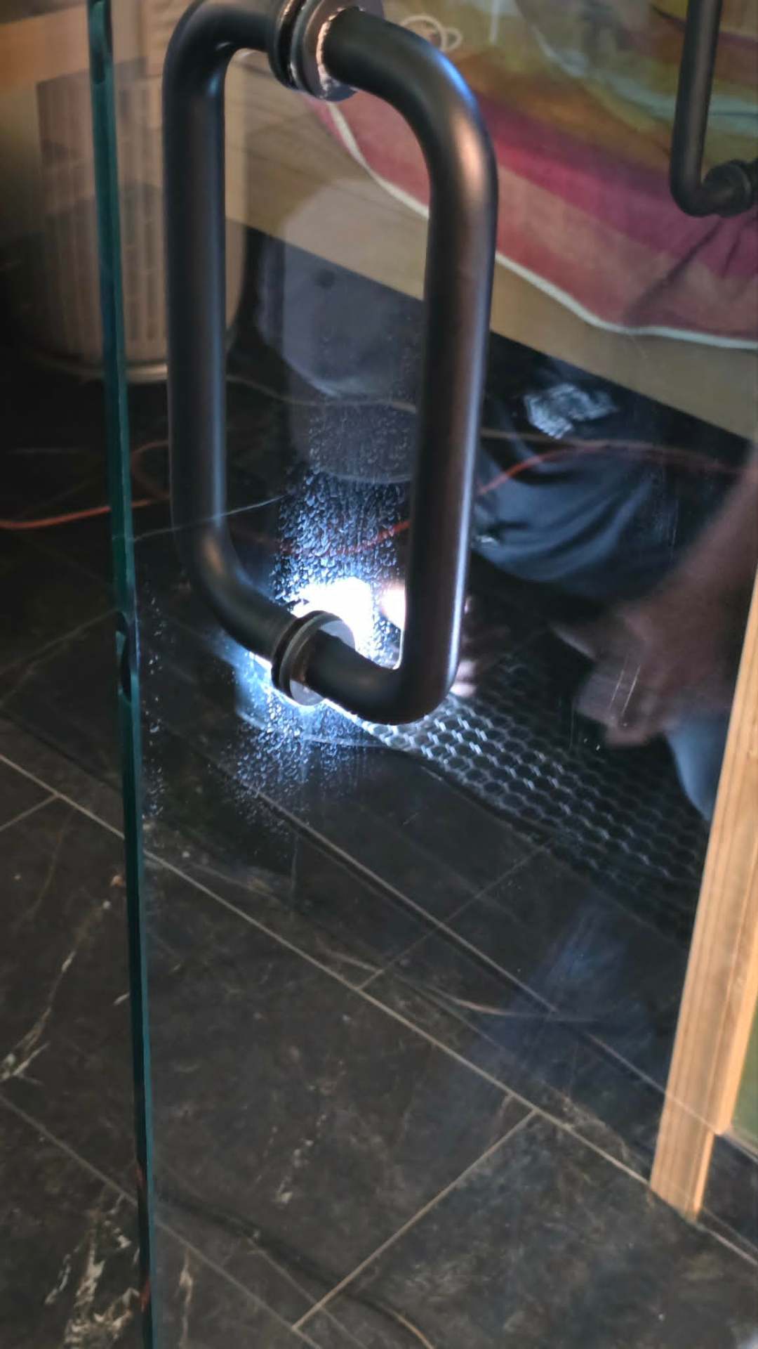 Close-up of a fully restored frameless glass shower door with oil-rubbed bronze handle on a dark marble tile floor in a Chandler Arizona bathroom showing crystal clear glass and beaded water after Lazona Tile Care cerium oxide polish and hydrophobic coating