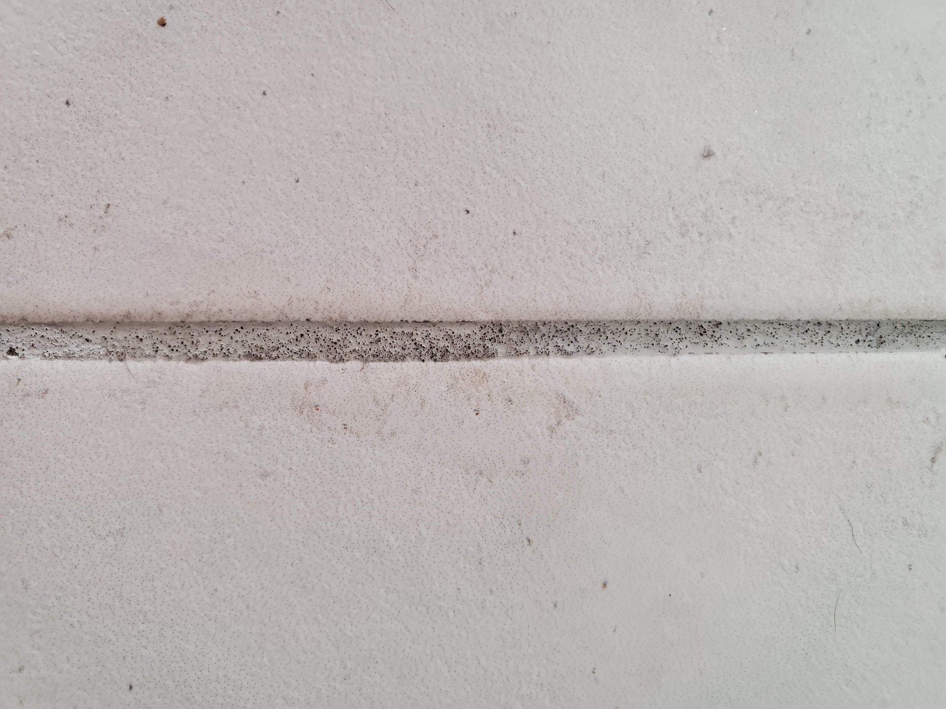 Powdery Grout in New East Valley Builds: Why It Happens and How to Fix It Close-up of powdery cement grout joint between white tile showing pinholes porous surface and dust residue caused by improper mixing and unneutralized grout haze remover in an Arizona new build