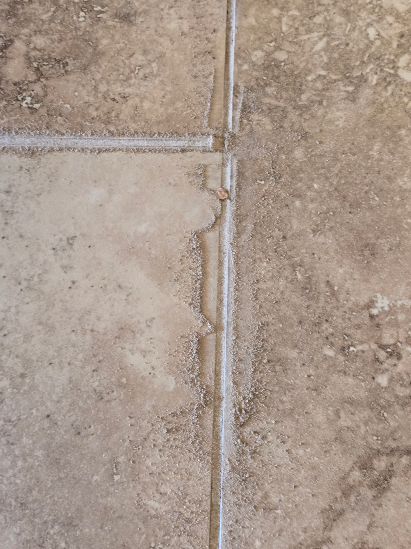 Travertine floor in an Arizona home showing white powdery efflorescence and eroded grout joints along tile edges caused by repeated vinegar mopping and unneutralized acidic cleaners